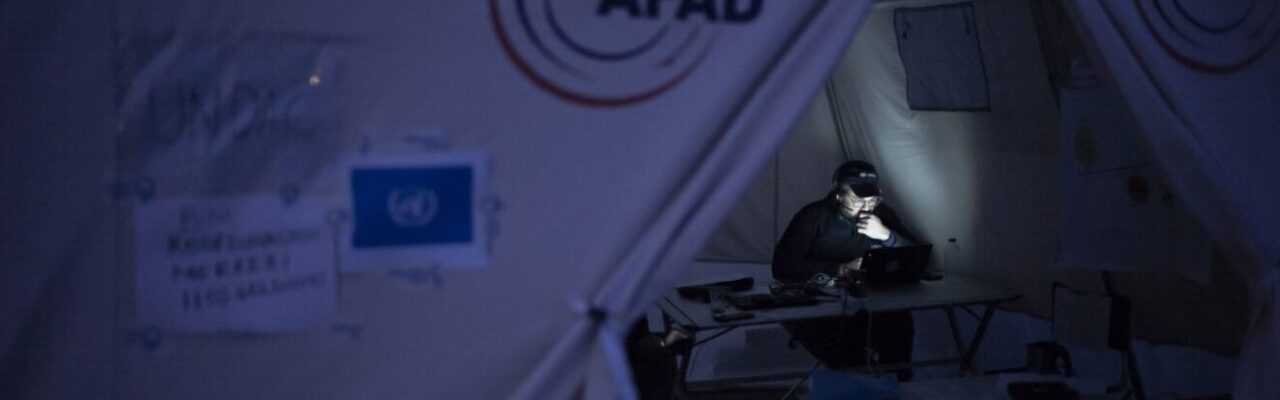 UNDAC member sitting in the On-Site Operations Coordination Centre (OSOCC) tent, working at night, Türkiye, 2023.