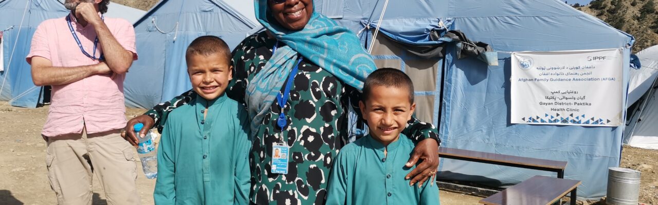 UNDAC member together with two children in front of a health clinic tent in Afghanistan.