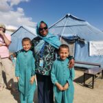 UNDAC member together with two children in front of a health clinic tent in Afghanistan.