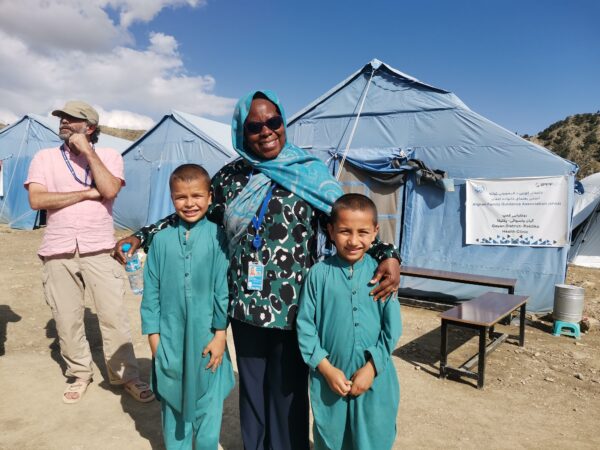 UNDAC member together with two children in front of a health clinic tent in Afghanistan.